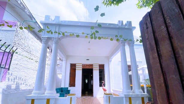 Un acceso cubierto con columnas blancas y un suelo de baldosas que conduce a una puerta.