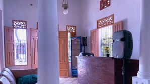 Una habitación con un mostrador de recepción de madera, una columna blanca grande, un sofá con cojines estampados y un suelo de baldosas.