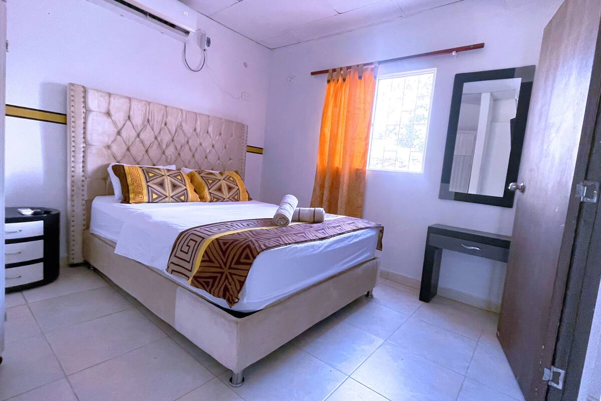 A hotel room with a large bed, a bedside table, a mirror, and a window with curtains.