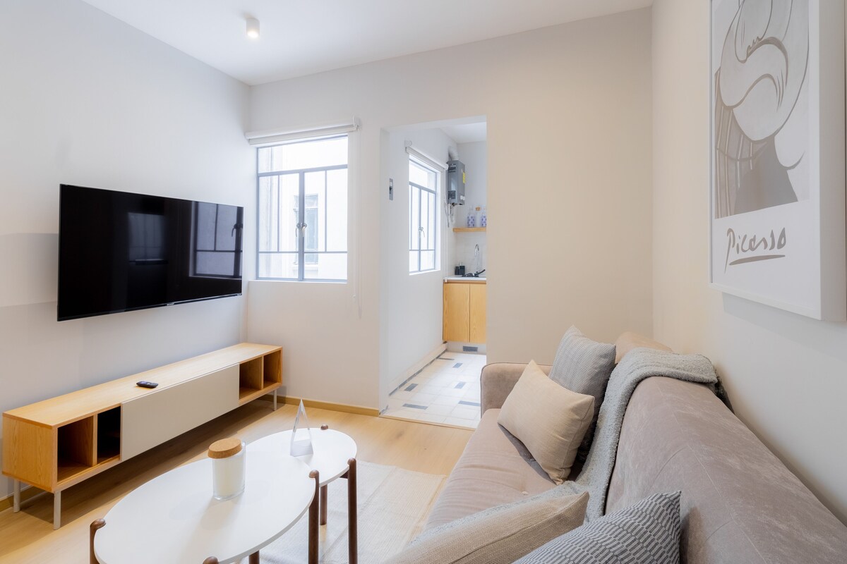 Una sala de estar moderna con una televisión de pantalla plana, una mesa de comedor redonda y un sofá.