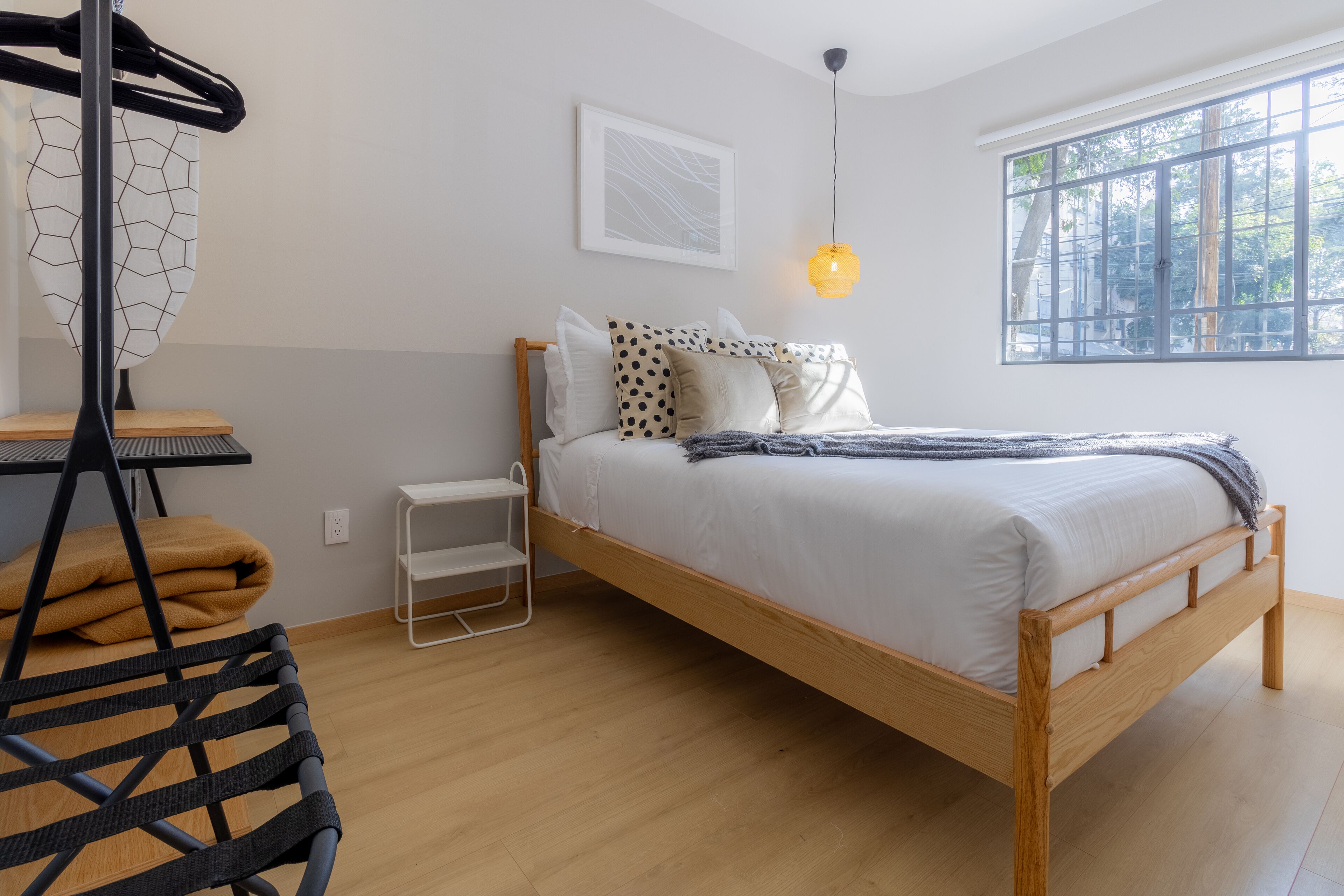 Quarto bem arrumado com cama de madeira, cadeira suspensa, mesa pequena e janela com vista para árvores.