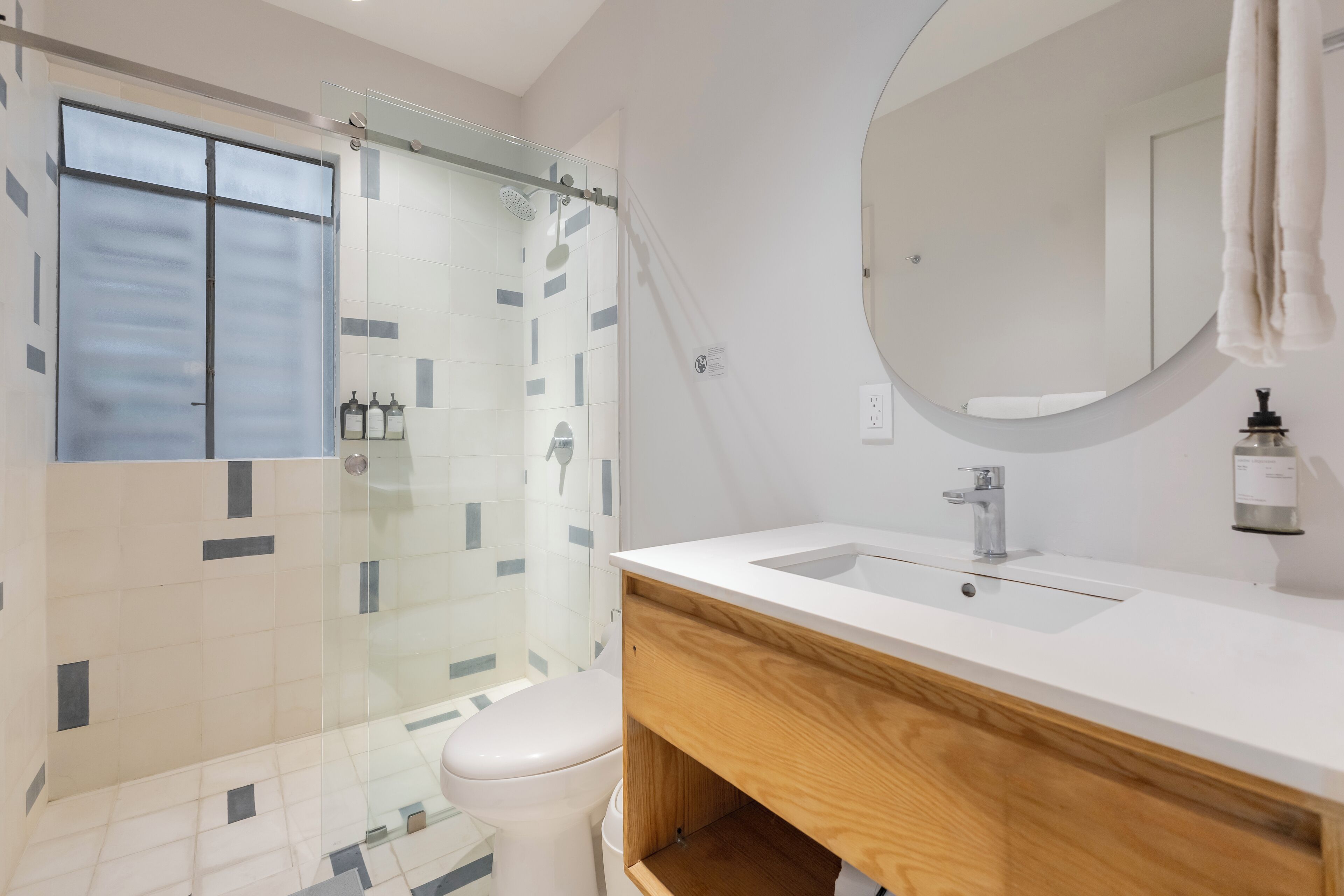 Une salle de bain moderne avec une douche à parois de verre, un lavabo blanc et un meuble-lavabo en bois.