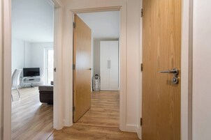 Un pasillo con suelo de madera, paredes blancas y un televisor en la habitación izquierda.