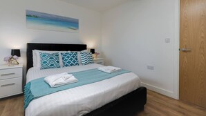 Un letto ben rifatto con cuscini decorati, una coperta turchese e un quadro appeso al muro.