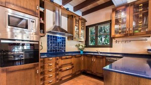 Eine Küche mit Holzschränken, einer Edelstahl-Mikrowelle, einer blauen Fliesenrückwand und einem Fenster mit Blick auf Bäume.