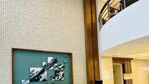 Un hall d’entrée moderne avec un plafond haut, une grande œuvre d’art abstraite au mur, un espace détente avec des canapés et des fauteuils, et un escalier menant à un niveau supérieur.