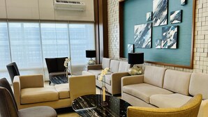 Un salon moderne avec un canapé beige, deux fauteuils, une table basse et une œuvre d’art accrochée au mur.