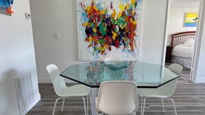 A modern dining area with a glass table and white chairs, a colorful abstract painting on the wall, and a bed in the background. - 2 Bedroom Longboat Key Beachside Paradise. Steps from the Beach! (Longboat Key)