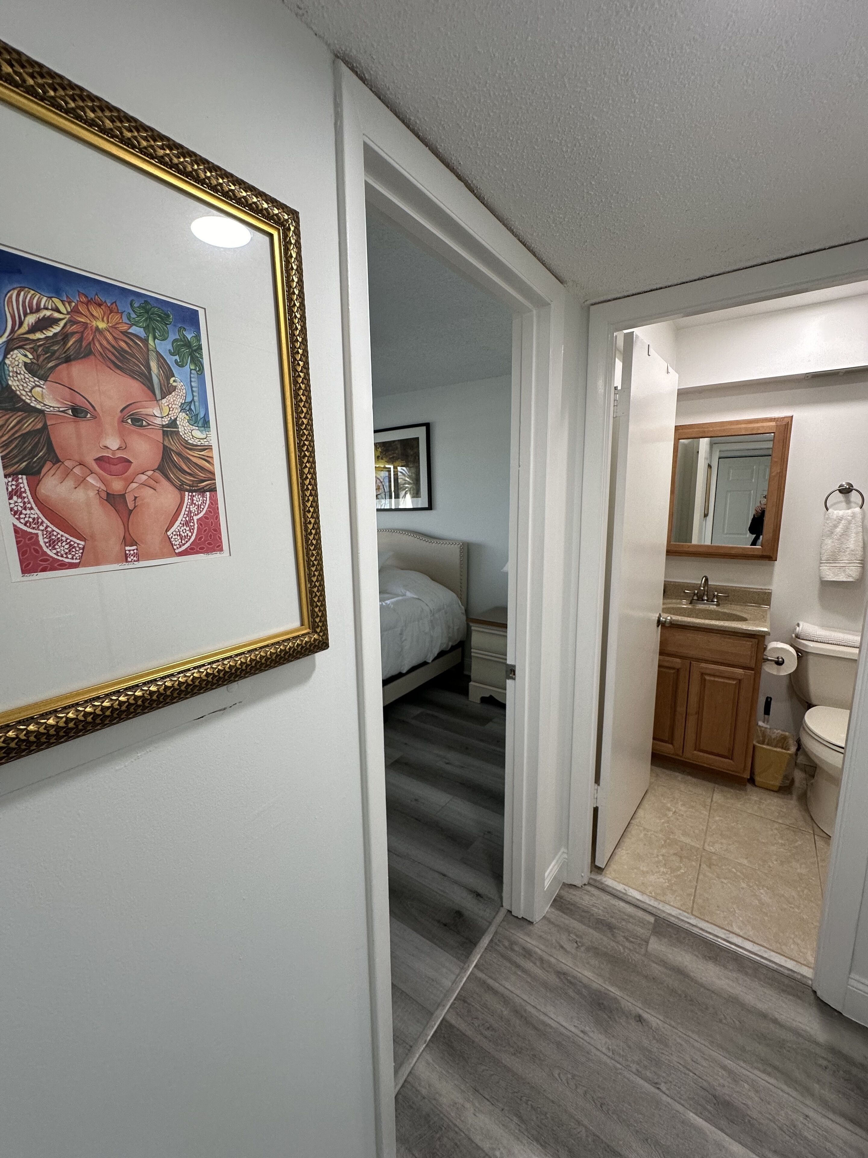 A hallway leading to a bedroom with a bed and a bathroom with a sink and toilet.