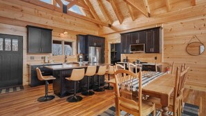 A wooden cabin interior with a kitchen, dining area, and bar seating. - Custom-Built Log Cabin with Long Range Views (Banner Elk)