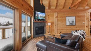 A cozy cabin interior with a fireplace, leather sofa, and a large window overlooking a snowy landscape. - Custom-Built Log Cabin with Long Range Views (Banner Elk)