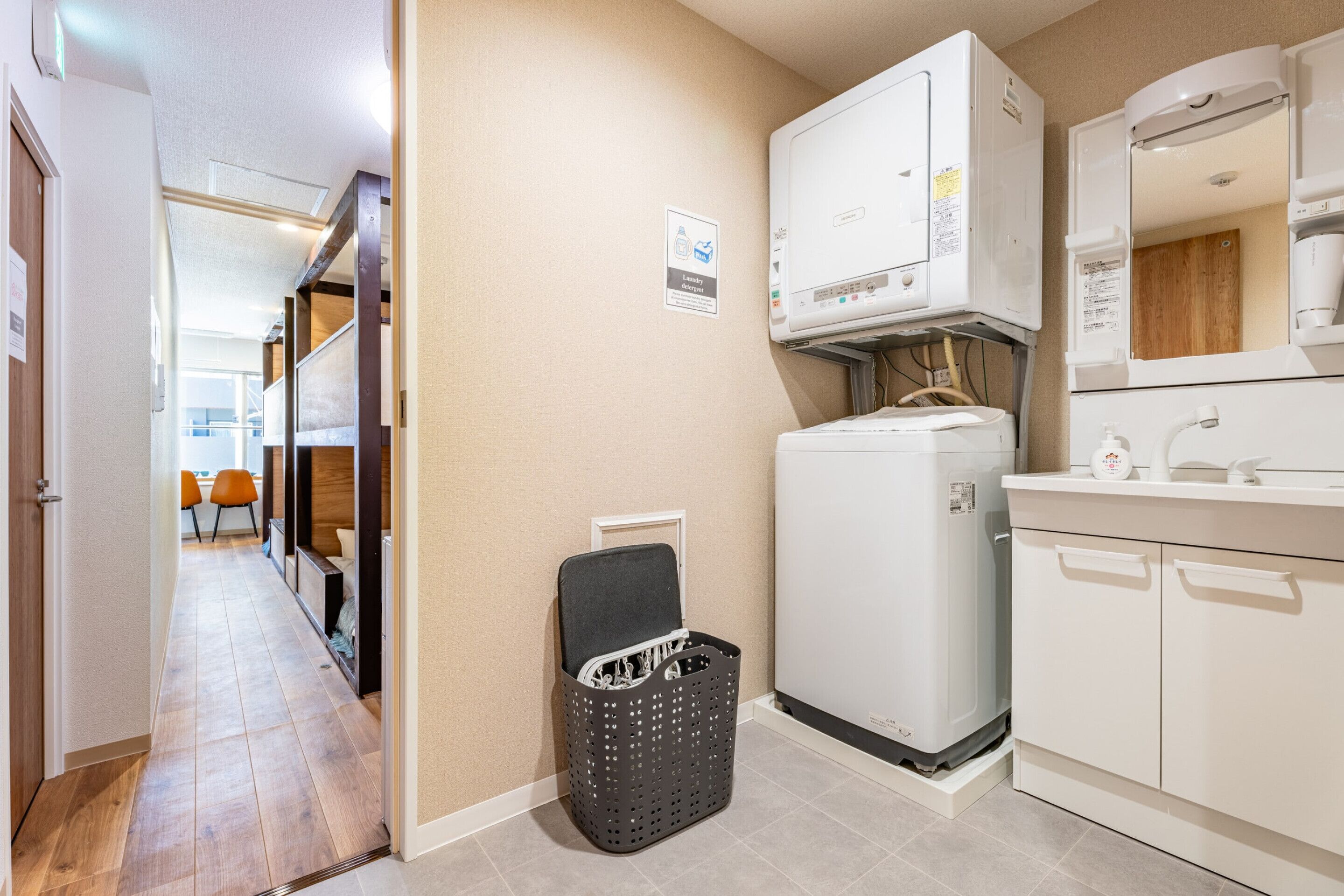 A compact kitchen with a refrigerator, microwave, and sink. A laundry basket is placed against the wall.