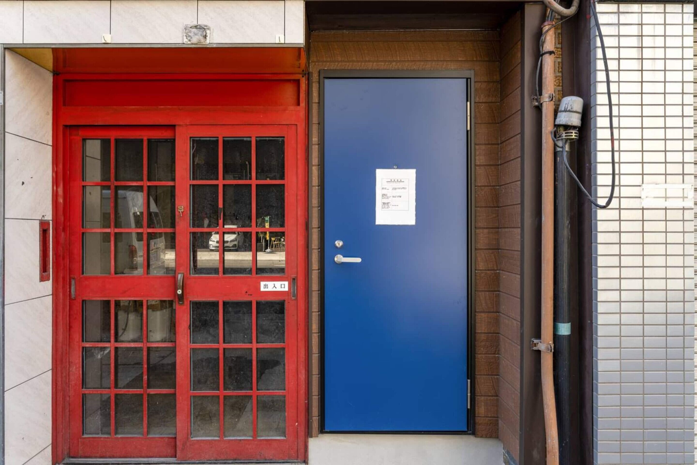 A red door with glass panels and a blue door with a sign.