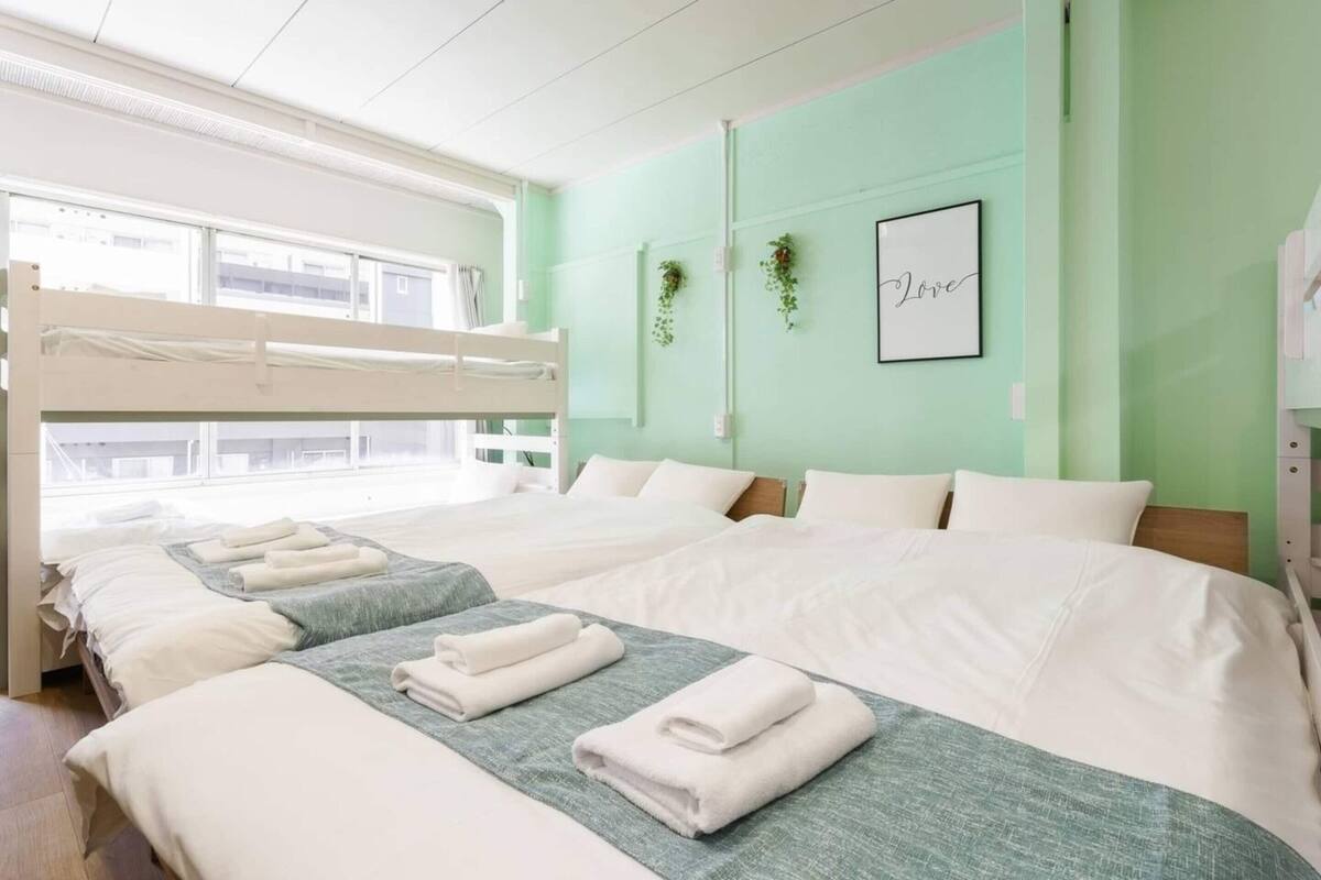 A hotel room with bunk beds, a large window, and a green wall with a framed picture and plants.