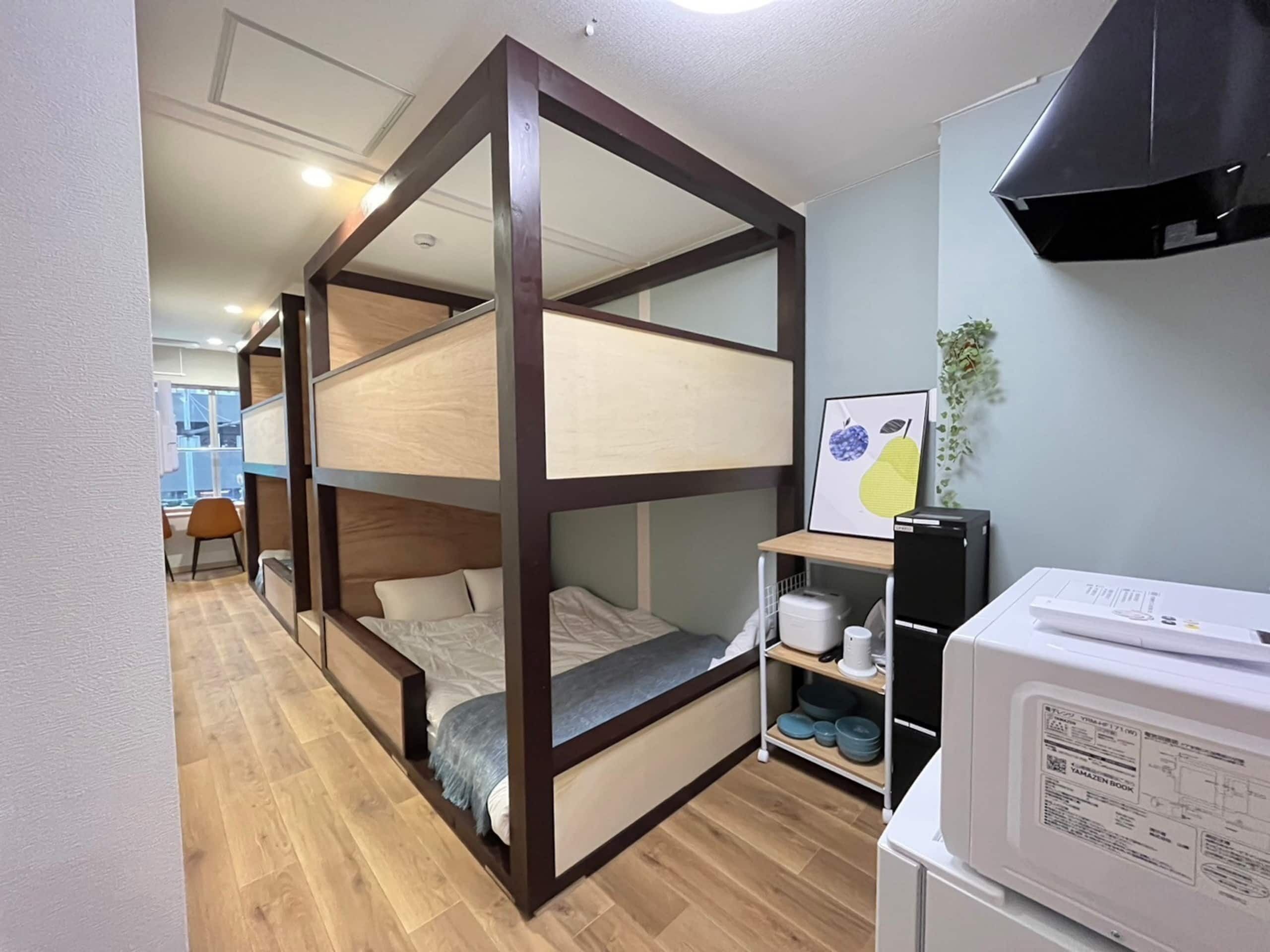 A compact room with a bunk bed, a small kitchenette with a microwave, and a dining area visible in the background.