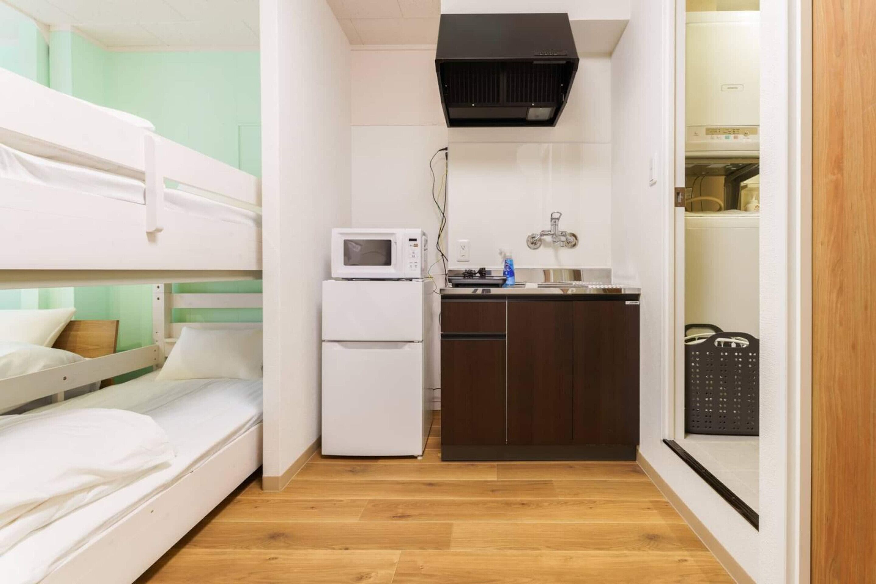 Ein kleines Zimmer mit Etagenbetten, einem weißen Kühlschrank, einer Mikrowelle, einem Waschbecken und einer schwarzen Dunstabzugshaube.
