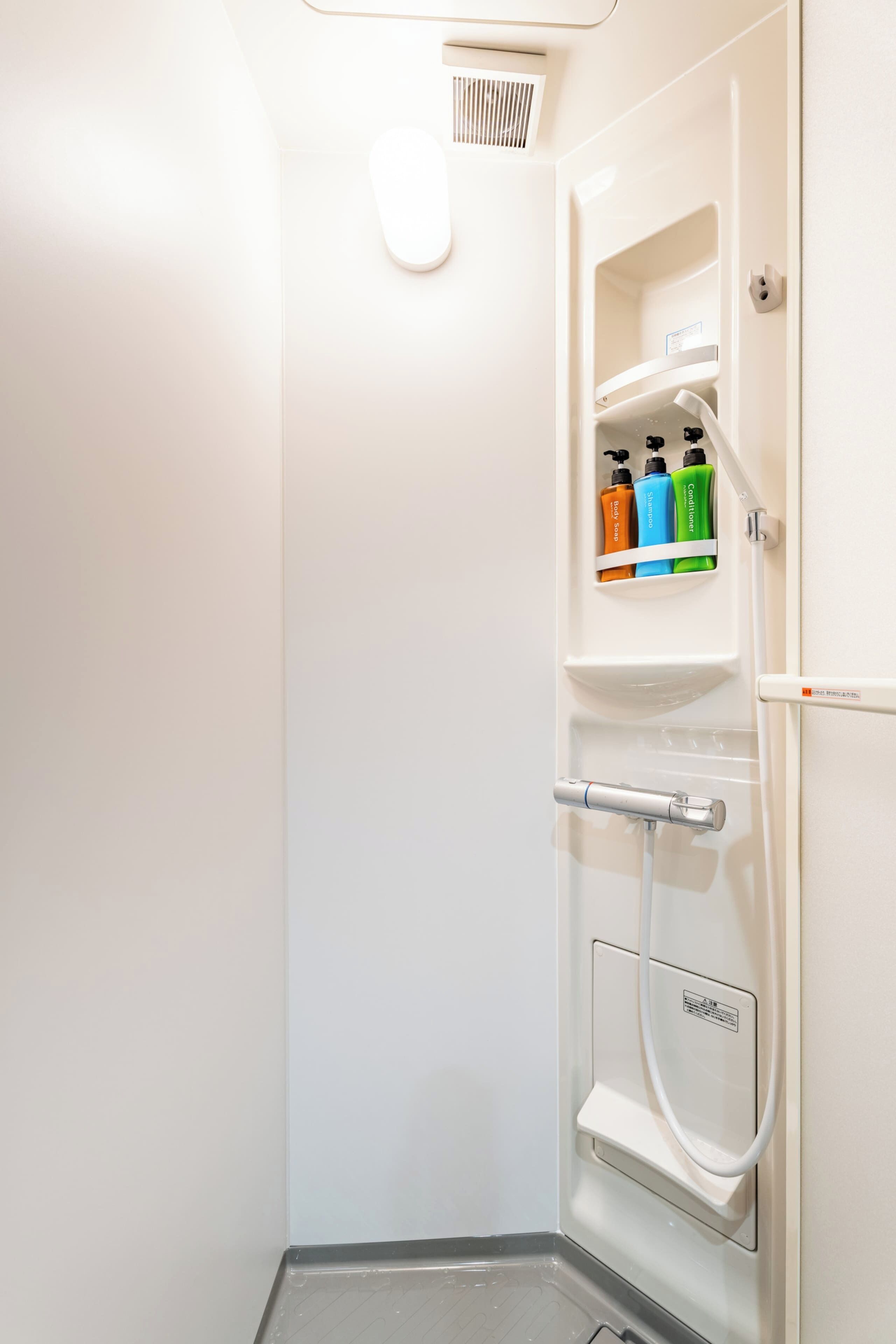 A bathroom with a shower, a hand dryer, and a shelf with toiletries.