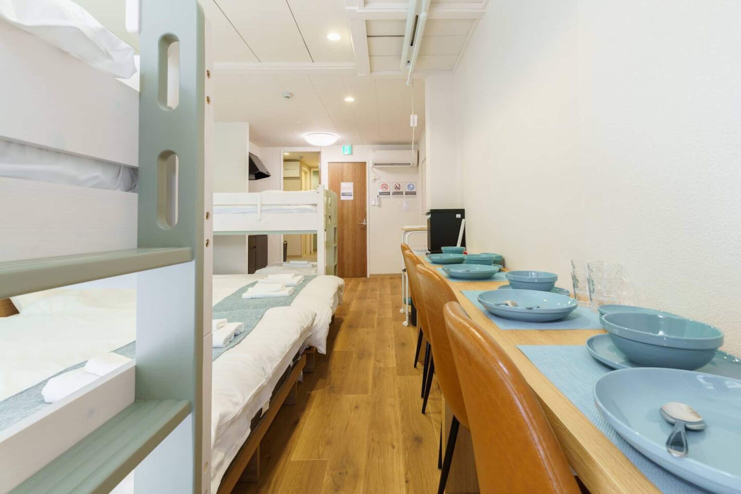 A hotel room with bunk beds, a wooden dining table with blue plates, and a TV on a stand.
