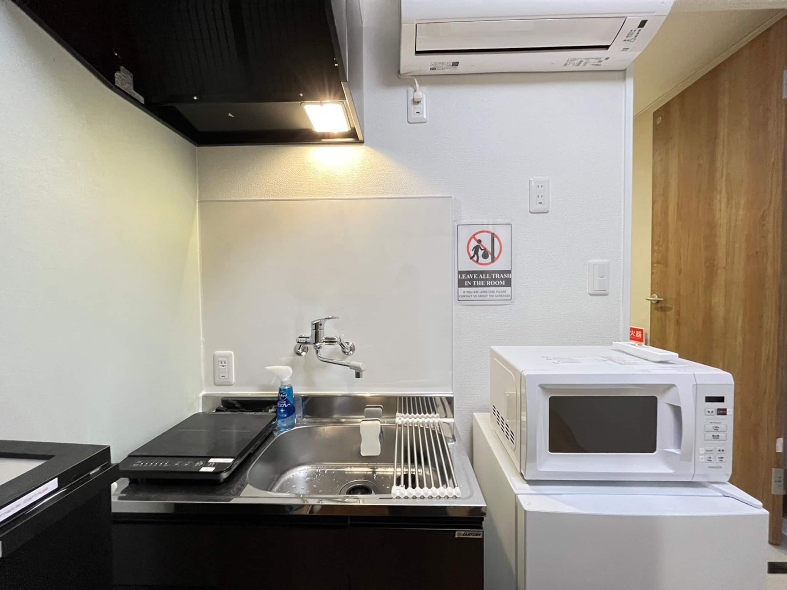 Una cocina con lavabo, grifo y microondas. Hay un cartel en la pared que dice 'Dejar toda la basura en la habitación'.