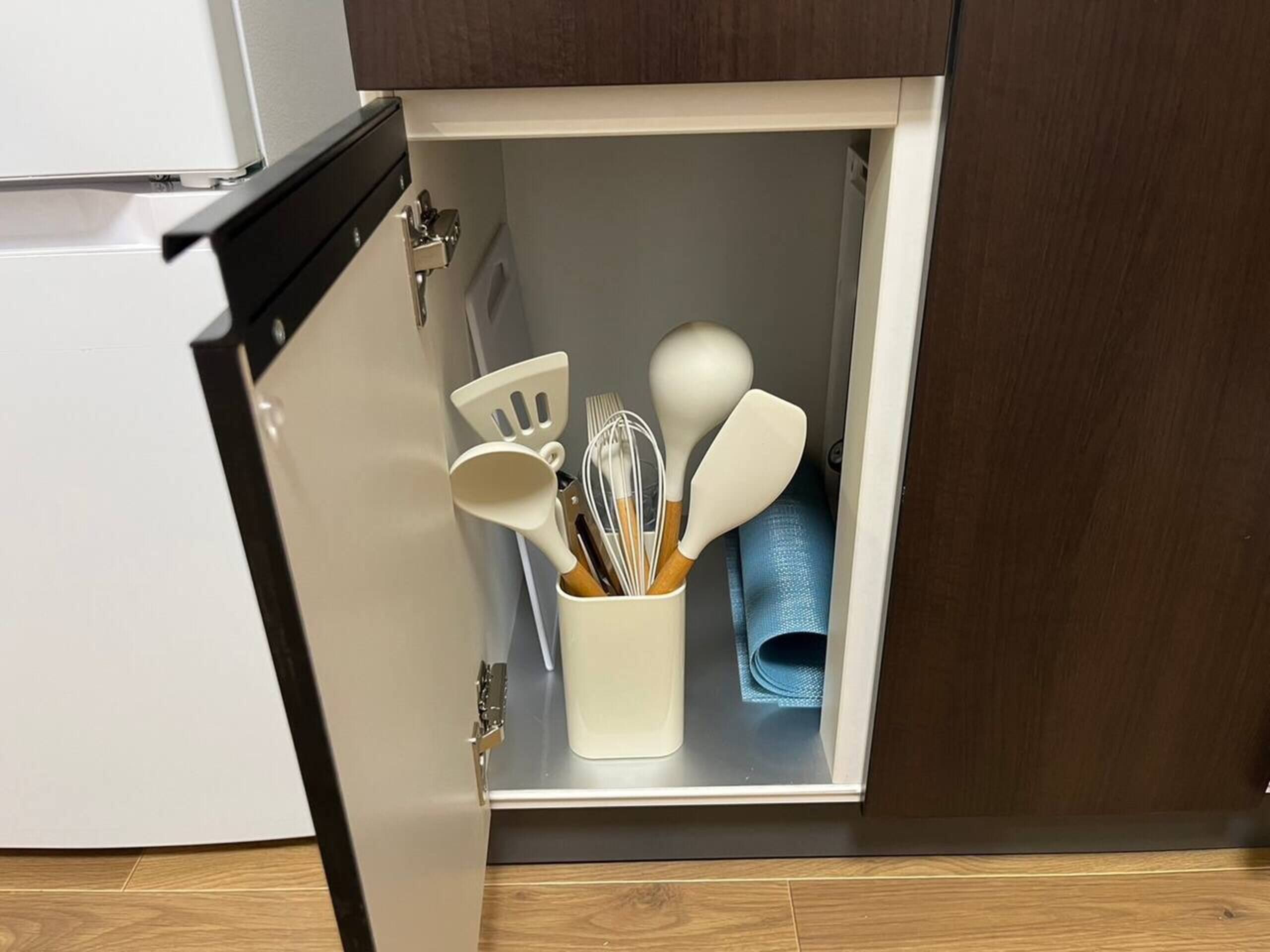 A kitchen cabinet with a white interior, containing a white container with kitchen utensils and a blue cloth.