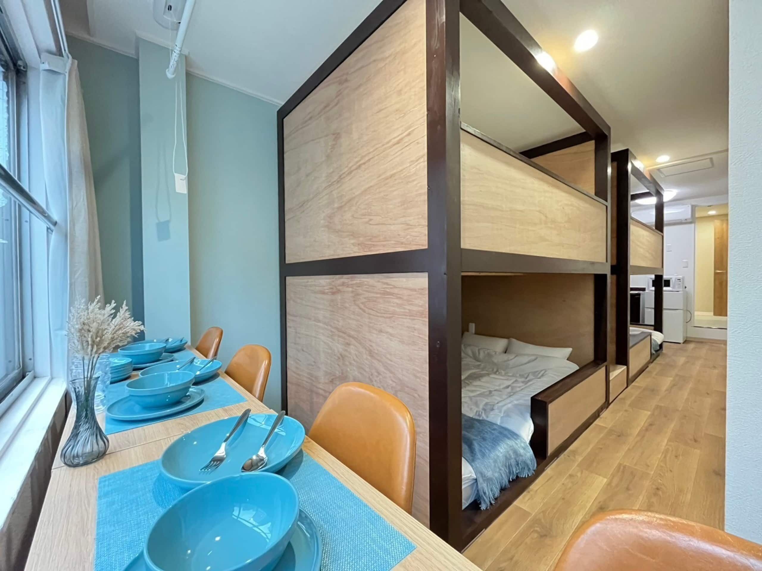 Una habitación de hotel compacta con literas, una zona de comedor con platos azules y una pequeña kitchenette.
