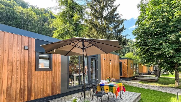 Un bâtiment moderne en bois doté d’une terrasse, de sièges extérieurs et d’un grand parasol.