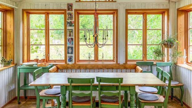 A dining area with a long wooden table and green chairs, large windows with a view of greenery, and a chandelier. - 2 bedroom nice home in Fjälkinge (Fjälkinge)