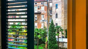 A view through a window with horizontal blinds, revealing a multi-story building with balconies and air conditioning units, surrounded by lush greenery. - 4 bedroom stunning apartment in Rijeka (Rijeka)