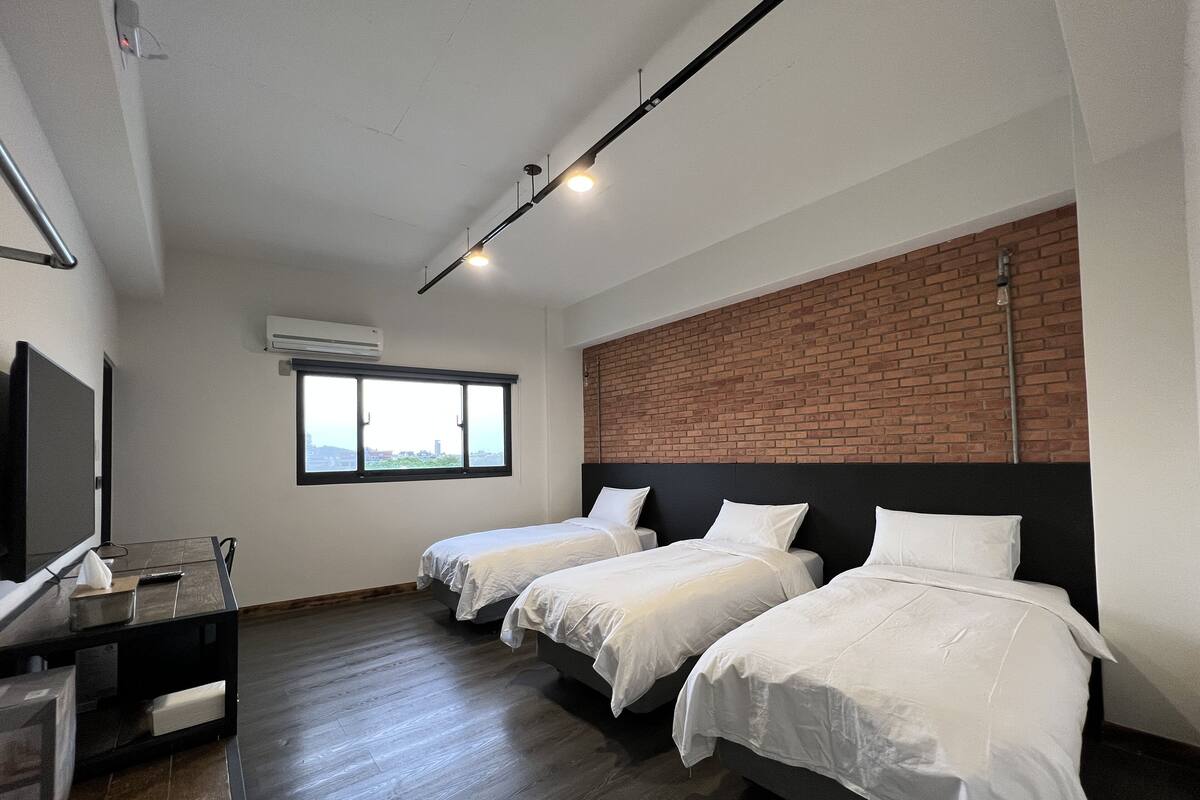 A hotel room with two single beds, a TV, a desk with a chair, and a window with a view.