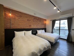 Habitación de hotel con dos camas, una pared de ladrillo y un ventanal con cortinas.