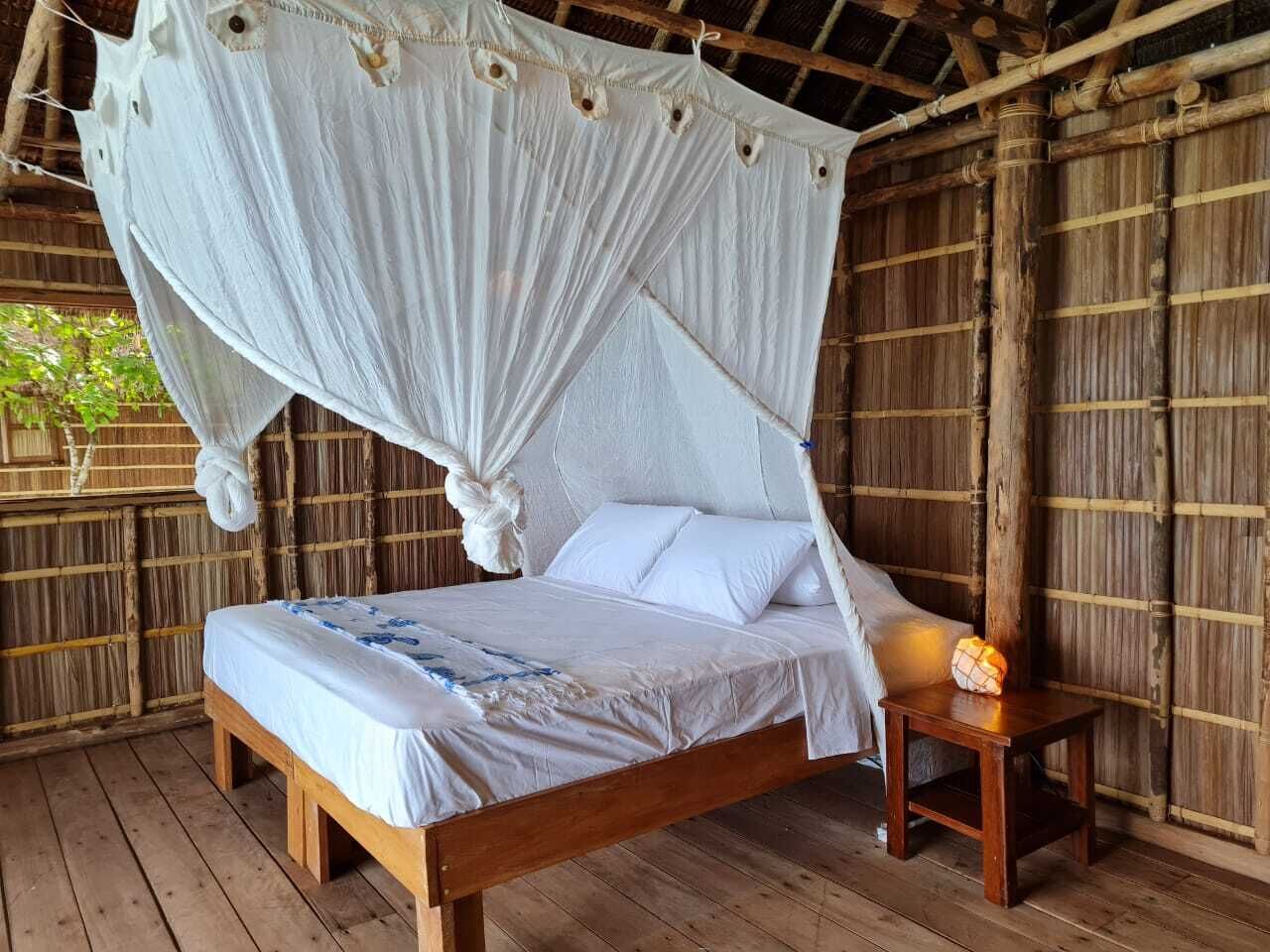 A wooden bed with a canopy, a bedside table with a lamp, and a bamboo wall.
