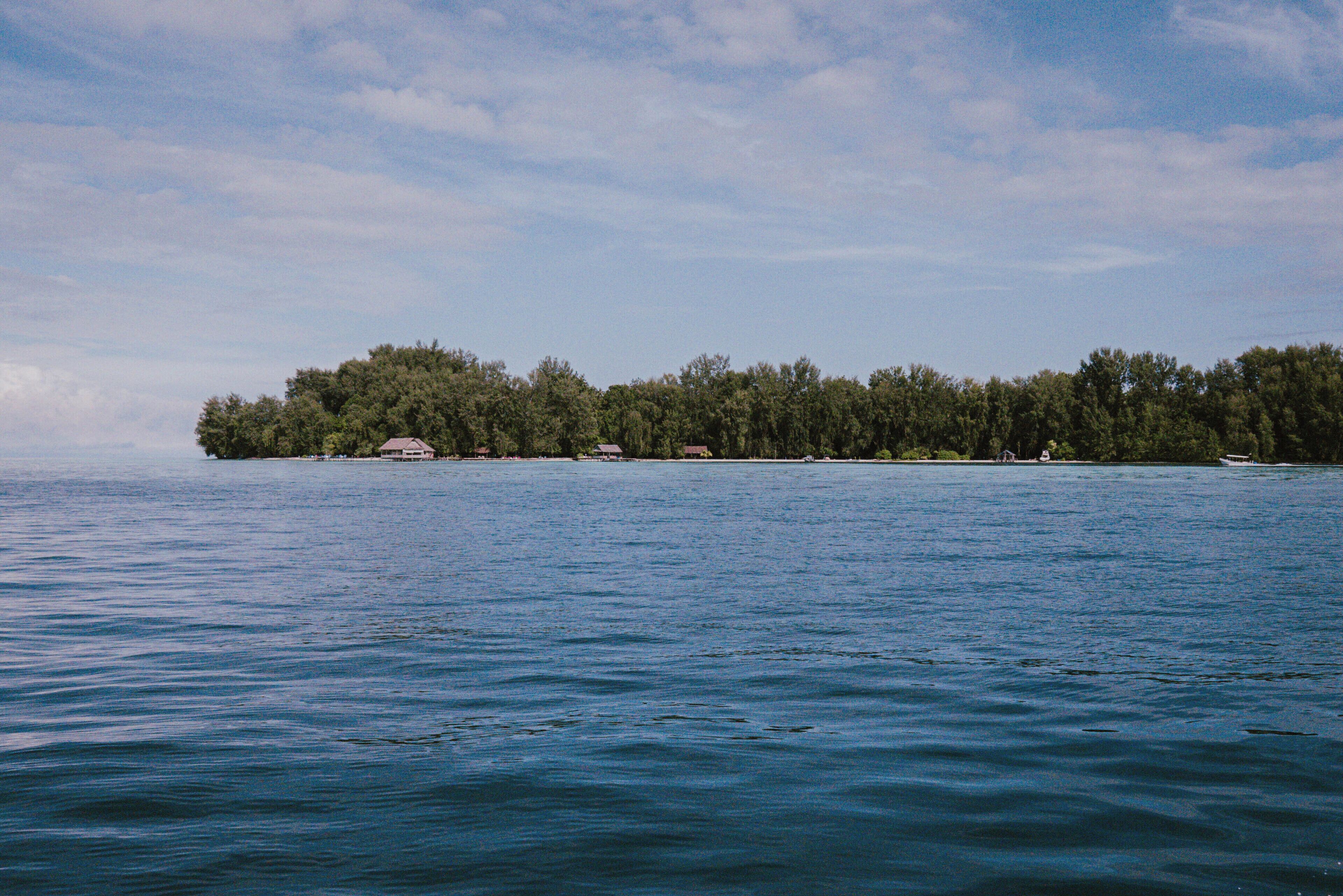 A calm body of water with a small island in the distance, surrounded by trees and a few buildings.