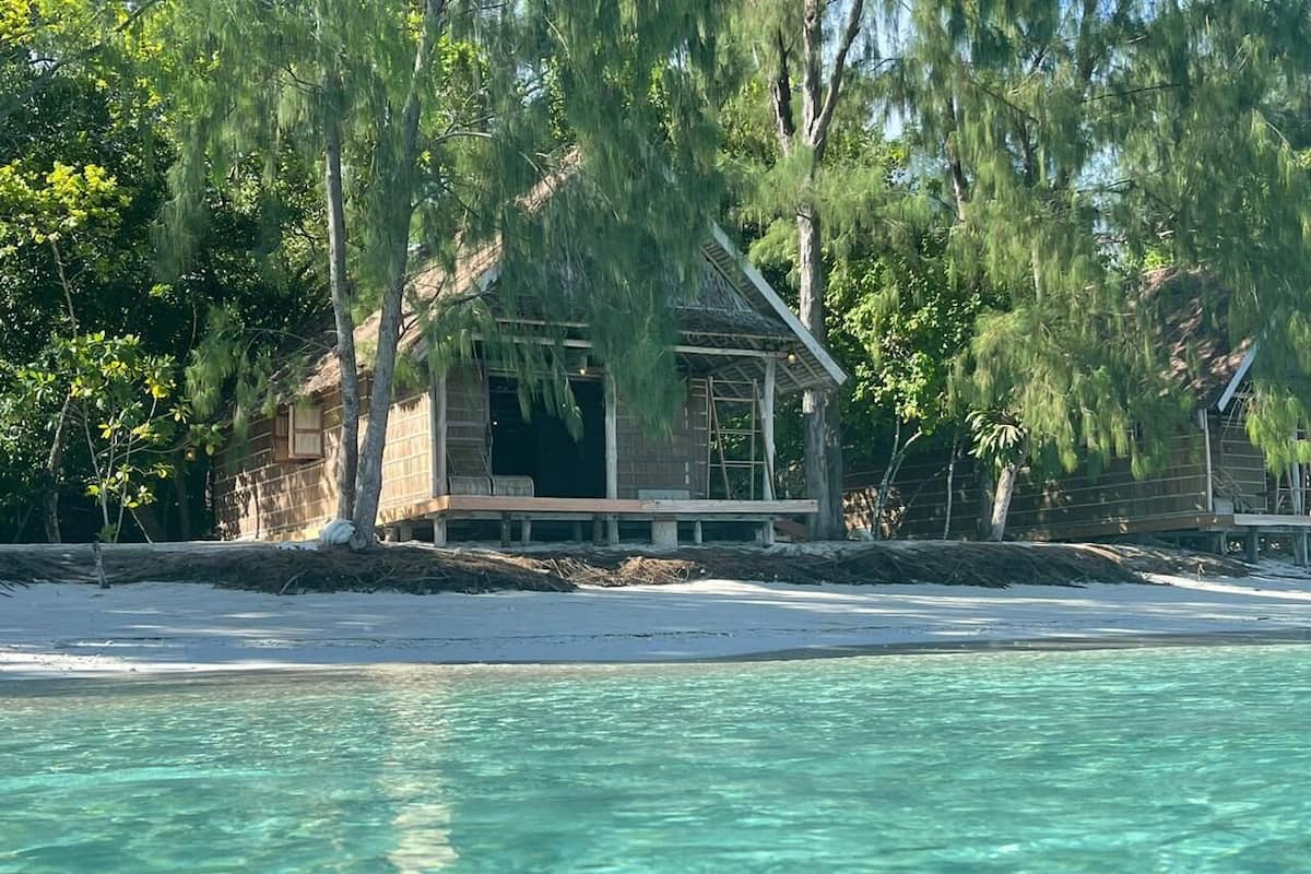 A beachfront property with a wooden structure, clear turquoise water, and surrounding trees.