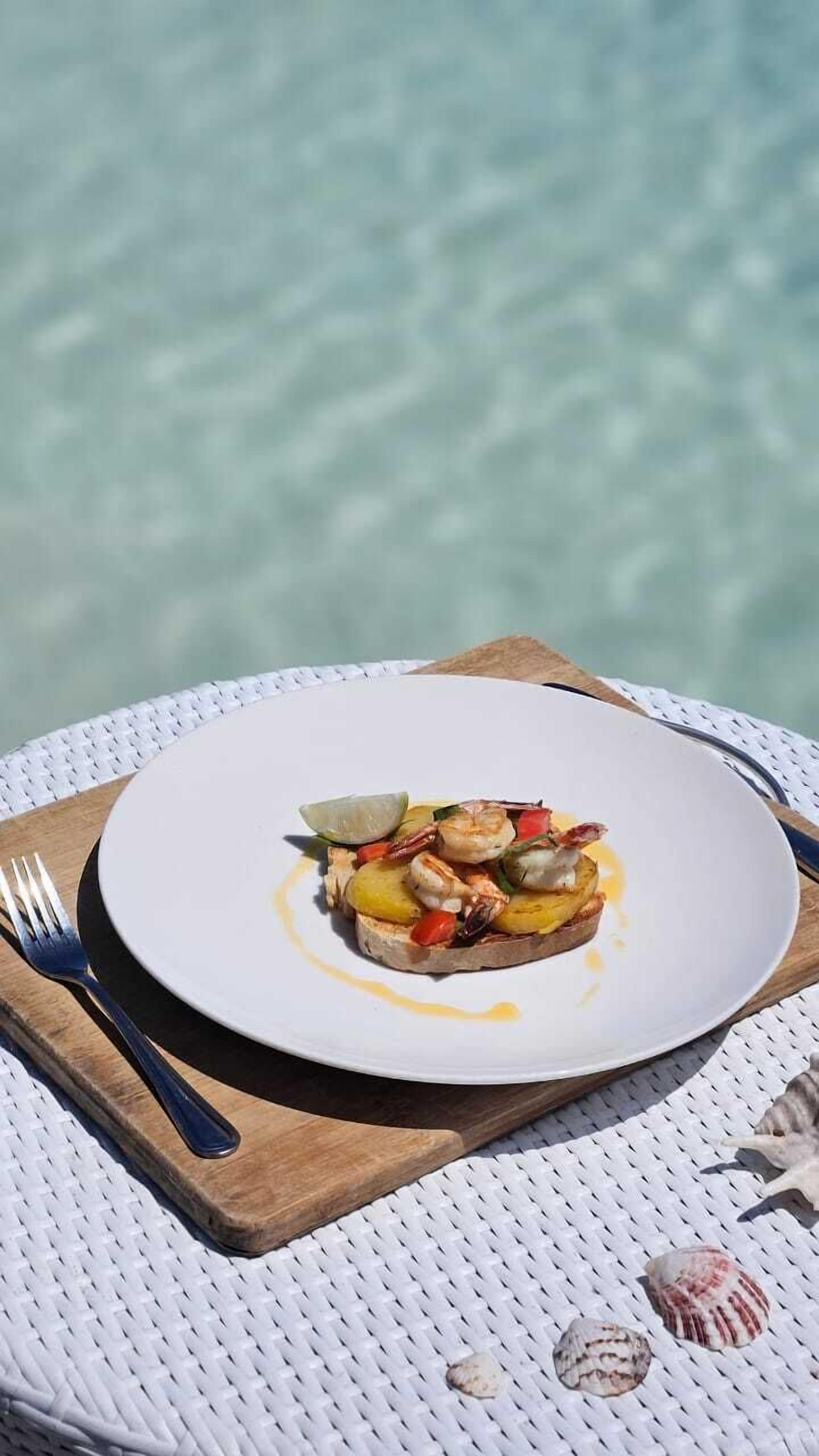 A plate of food on a white table with a wooden board underneath, set on a white wicker tablecloth.