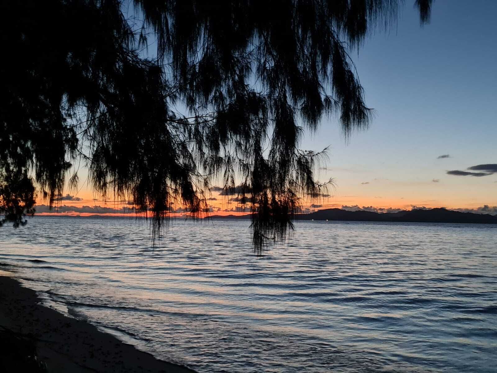 Une plage avec une eau calme et un coucher de soleil en arrière-plan.