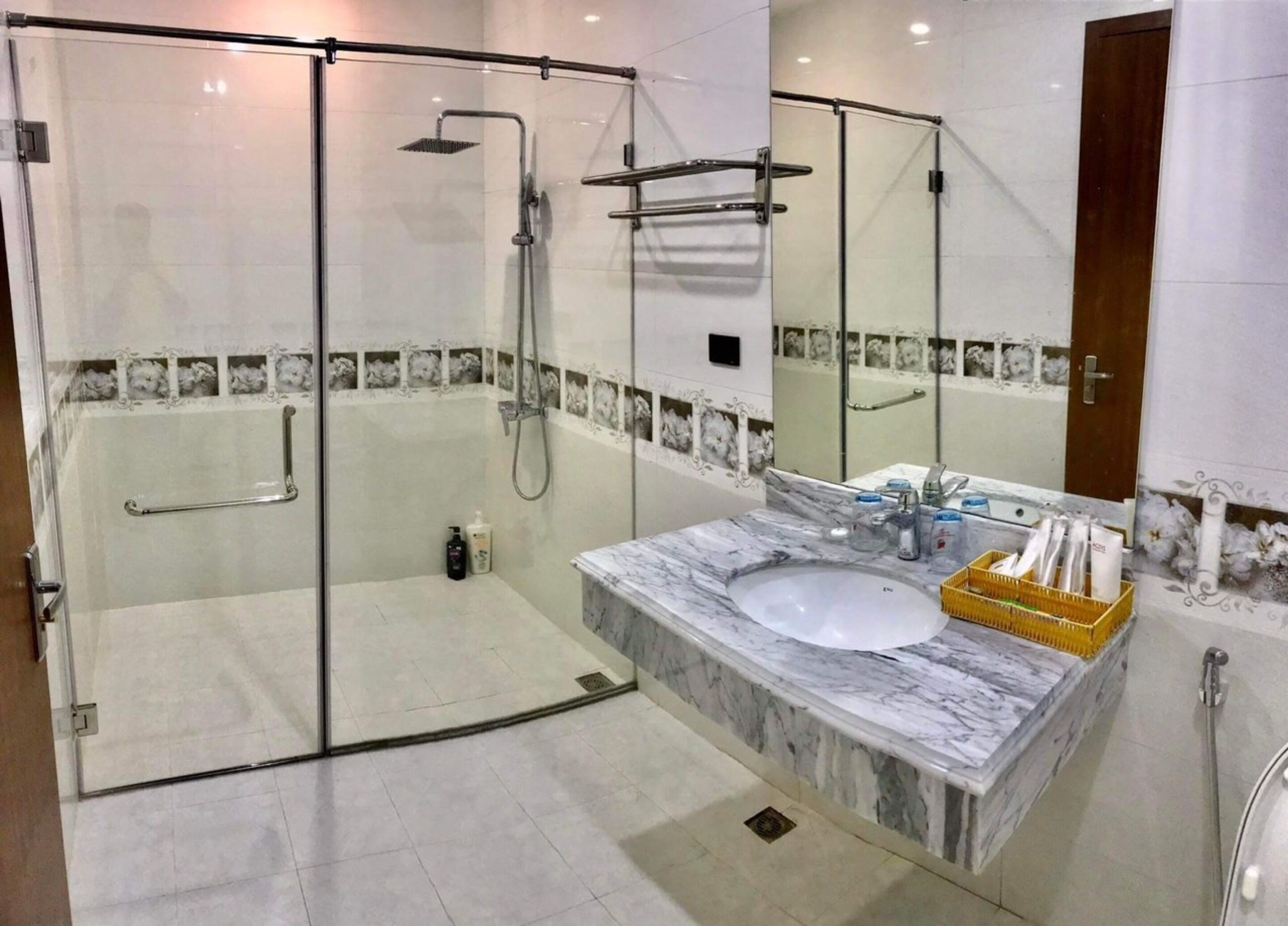 A modern bathroom with a glass-enclosed shower, a marble sink, and a mirror.