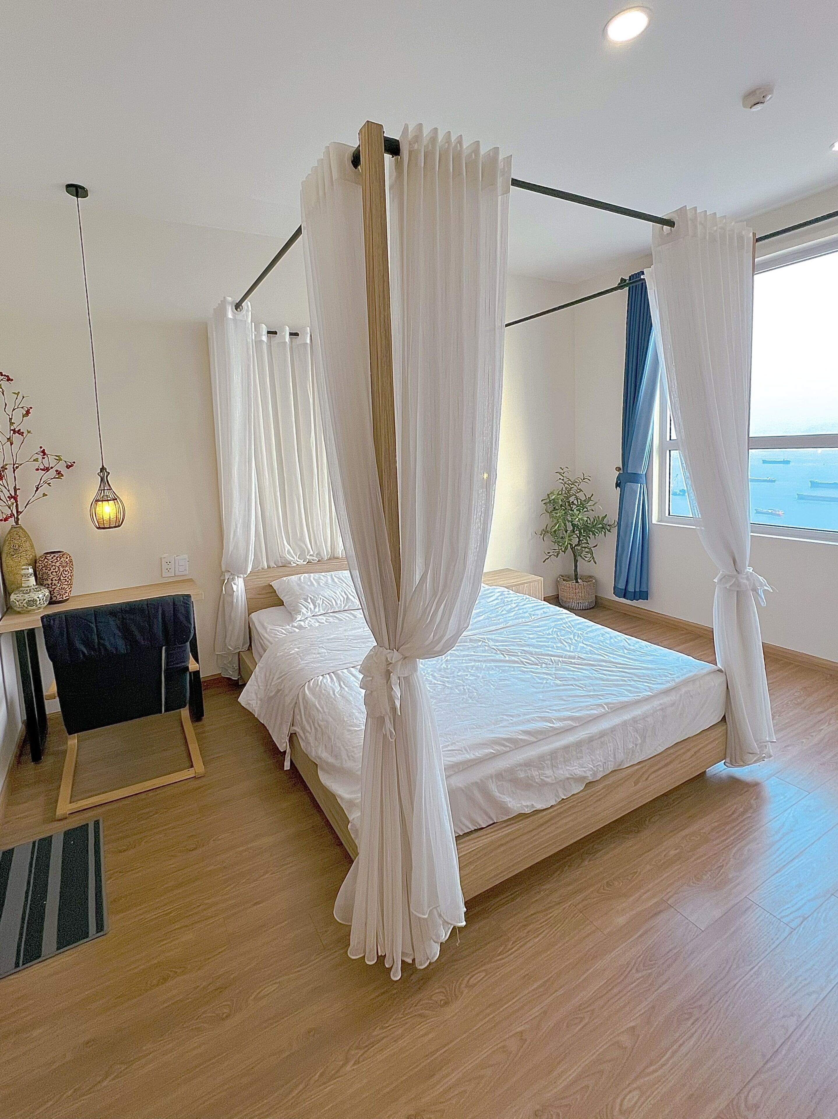 Ein geräumiges Schlafzimmer mit einem großen Bett, weißen Vorhängen, einem Nachttisch mit Lampe und Meerblick.