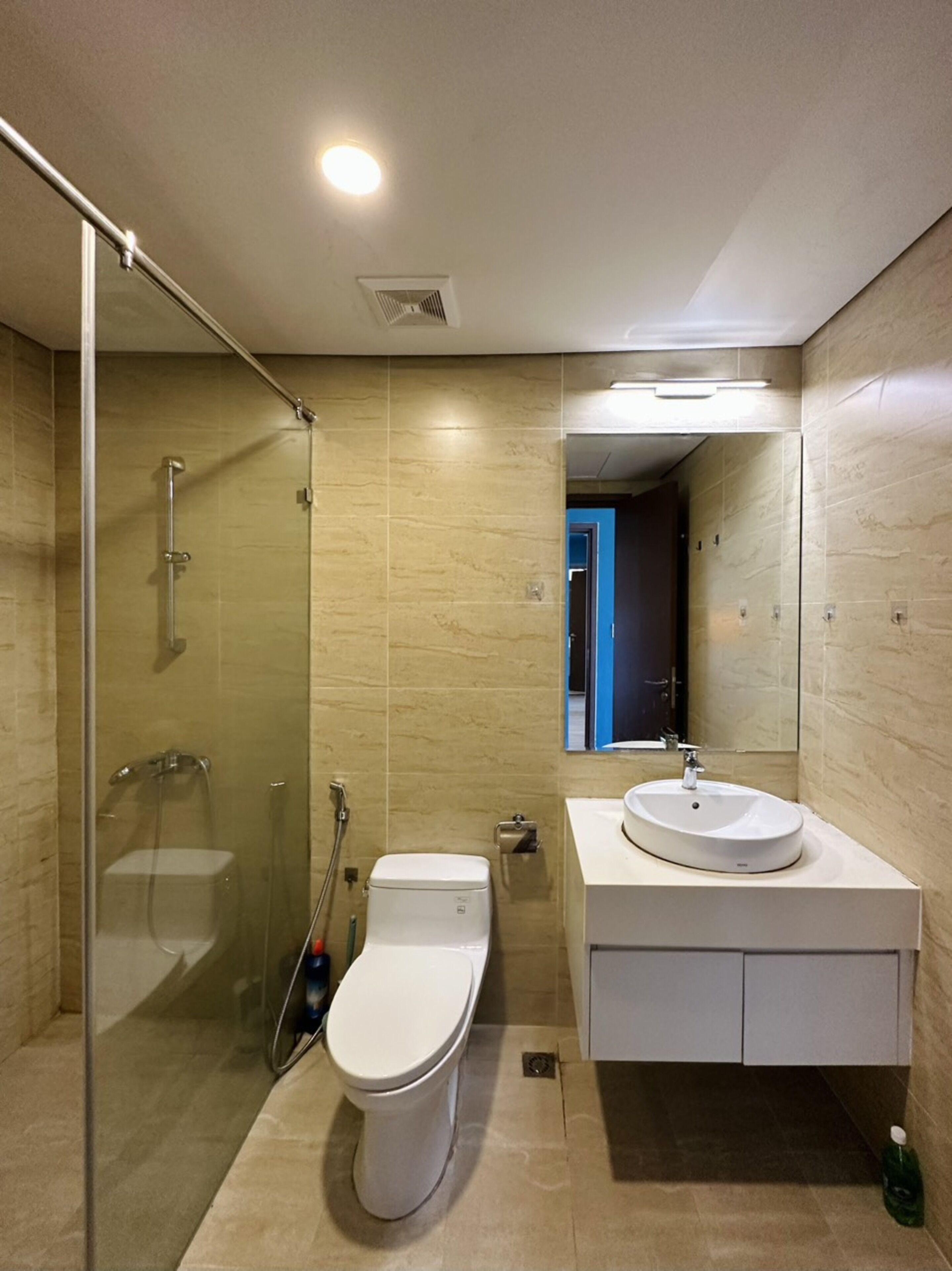 Un baño moderno con ducha de vidrio, inodoro blanco y lavamanos redondo con espejo.