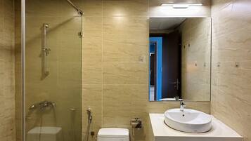 Un baño moderno con ducha de vidrio, inodoro blanco y lavamanos redondo con espejo.