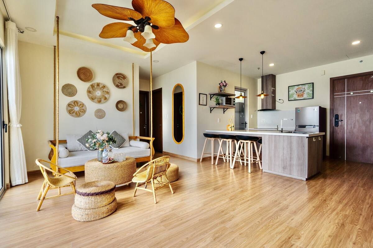 A modern kitchen with a central island, wooden flooring, and a dining area with wicker furniture.