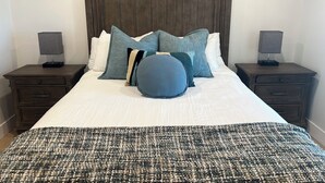 A neatly made bed with a dark headboard, two bedside tables with lamps, and two framed pictures on the wall.