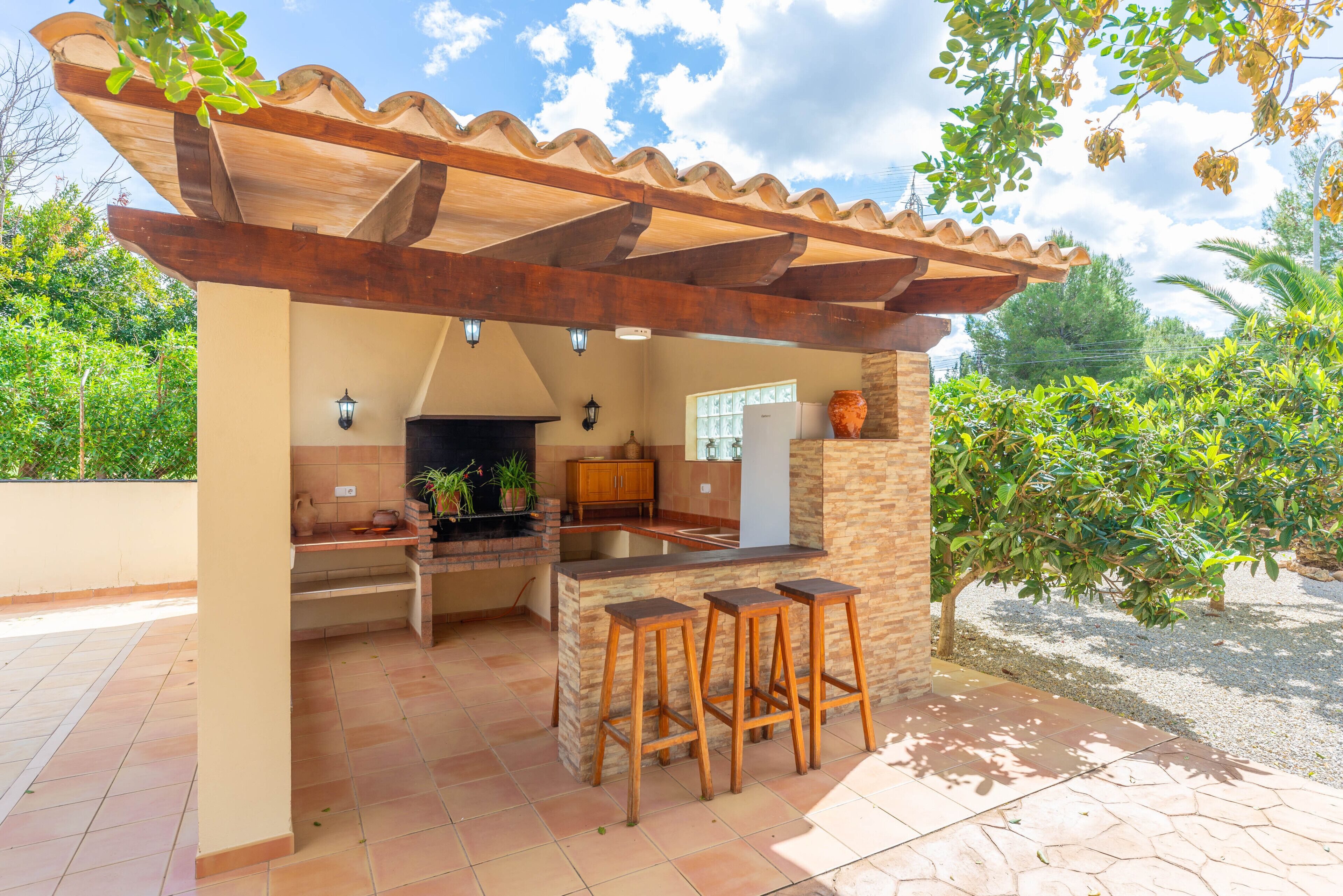 Une cuisine extérieure dotée d’un îlot en pierre, de tabourets en bois et d’une pergola.