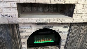 A stone fireplace with a built-in TV screen displaying a fireplace simulation. - Home in Miami Gardens (Miami)