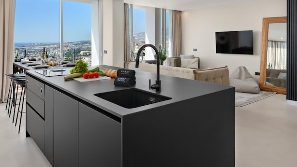 A modern kitchen with a large island, bar stools, and a view of the city. - Karat Villa Sand Torviscas (Costa Adeje)