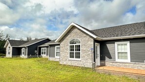 A row of modern houses with stone facades and dark siding, set in a grassy area with a clear sky. - Executive PEI Getaway Near Golf and Beaches for Groups or Families (Stanley Bridge)