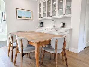Un comedor con una mesa de madera y cuatro sillas, una cocina con armarios blancos y un cuadro en la pared.