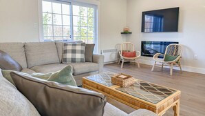 A living room with a sofa, two wicker chairs, a glass coffee table, and a flat-screen TV mounted on the wall. - Executive PEI Getaway Near Golf and Beaches for Groups or Families (Stanley Bridge)