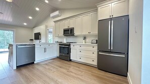 A modern kitchen with white cabinetry, stainless steel appliances, and a wooden floor. - Executive PEI Getaway Near Golf and Beaches for Groups or Families (Stanley Bridge)