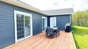 A deck with a table and chairs, a covered grill, and a door with a window. - Executive PEI Getaway Near Golf and Beaches for Groups or Families (Stanley Bridge)