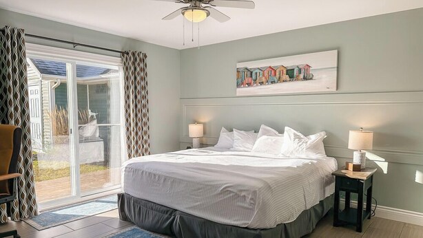 A bedroom with a bed, two bedside lamps, a ceiling fan, a window with curtains, and a painting on the wall. - Home Away Villa: Ideal for Island Adventures (Stanley Bridge)